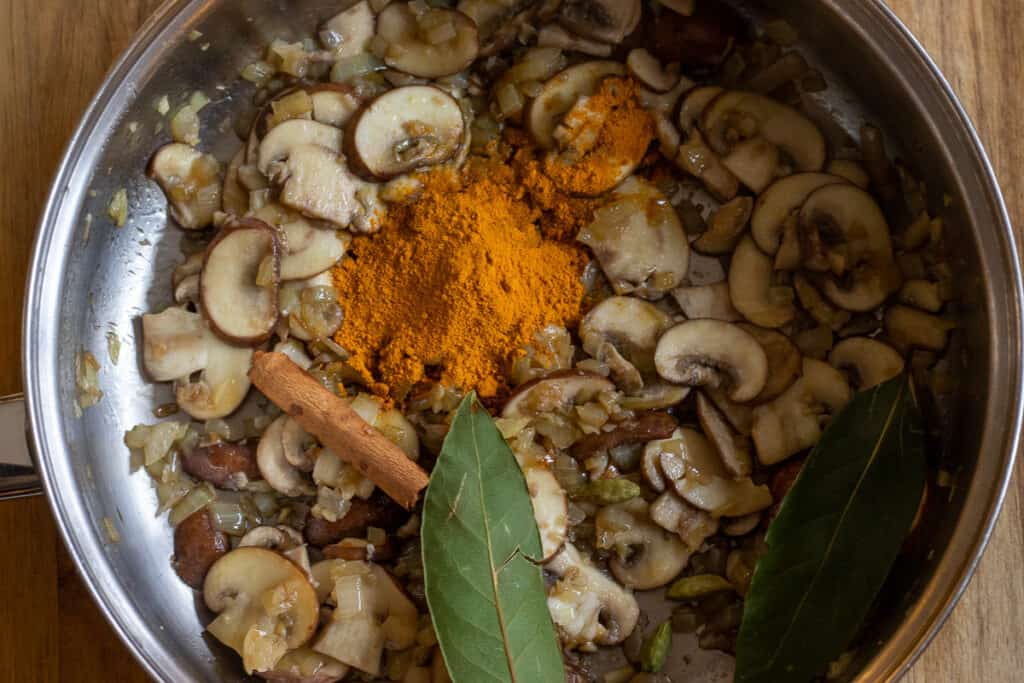 Turmeric, cinnamon stick, and bay leaves added to the sauteed mushrooms and onions.