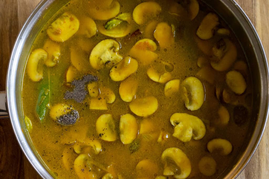 Golden turmeric stock poured over the mushrooms and spices in the pan.