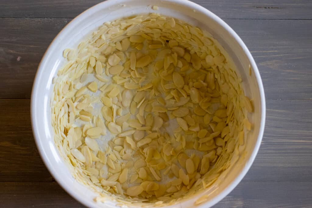 The sides and the bottom of an oven dish are buttered and lined with almonds.