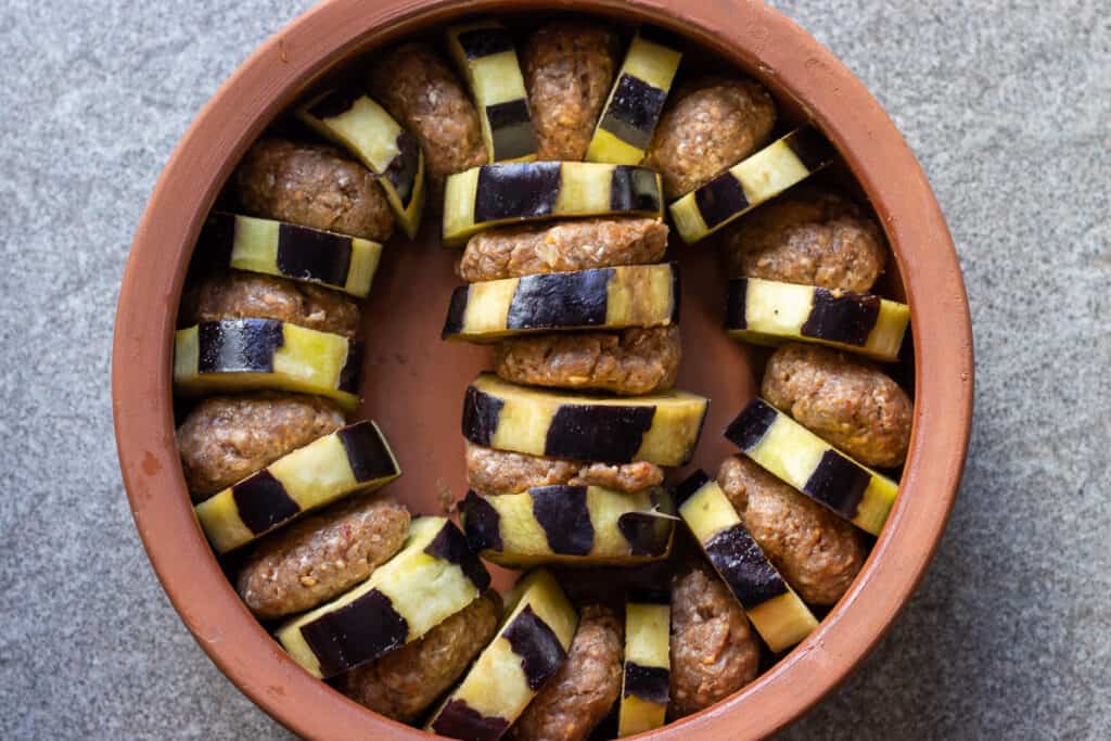The meatballs and eggplant slices arranged upright in an oven dish.