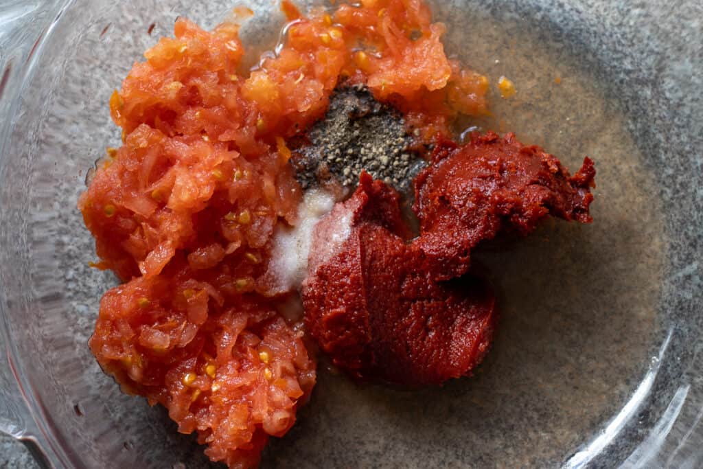 Grated tomato, tomato paste, and seasoning in a bowl.