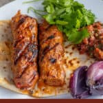 Two grilled Adana kebab skewers on flatbread with parsley and red onion.