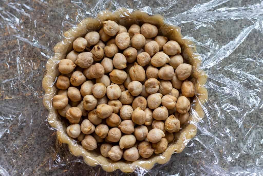 A tartlet shell lined with cling film and filled with chickpeas for blind baking.
