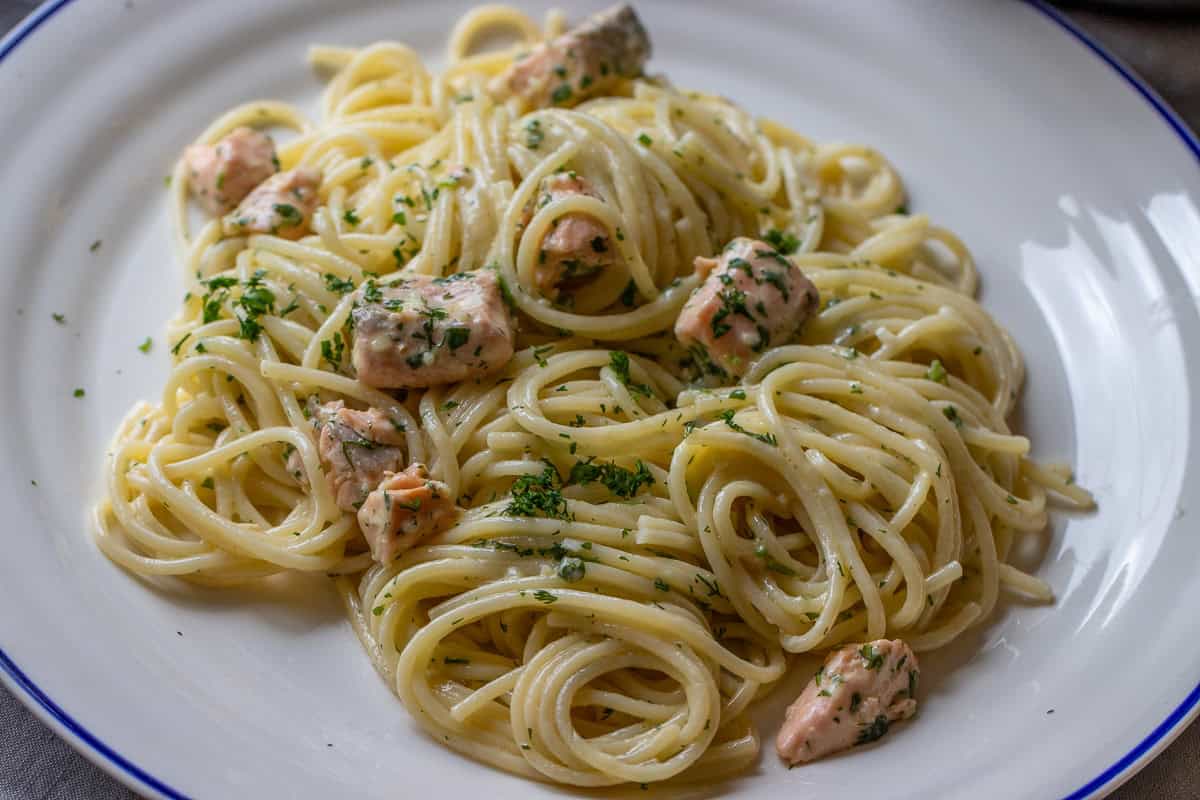 Pasta alfredo made with salmon is served with fresh herbs on a plate.