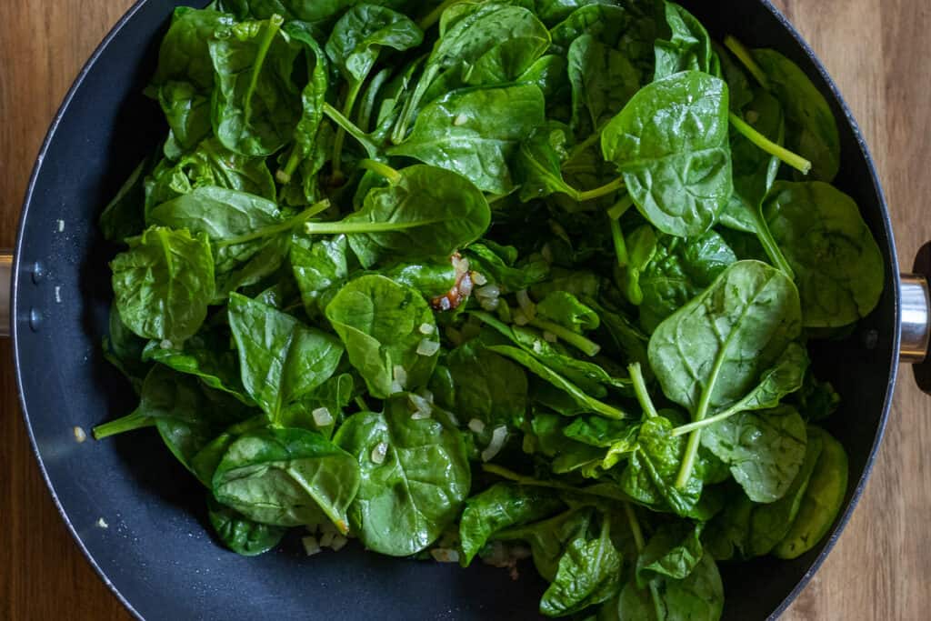 Sautéing the spinach in a wok with the onions.