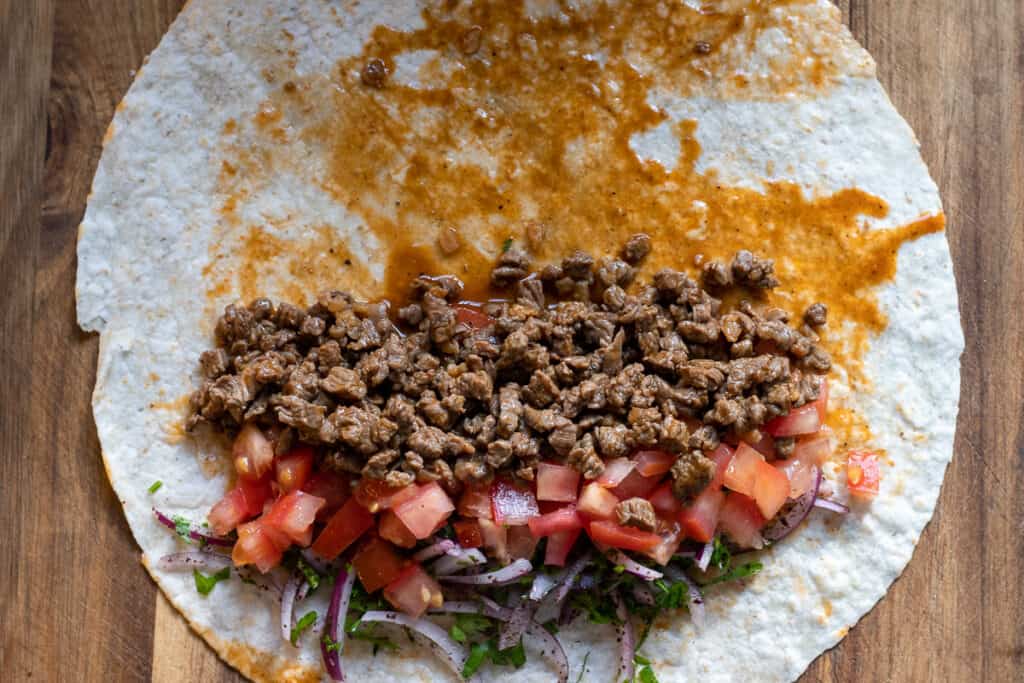 2 tablespoons of cooked beef, tomatoes, and onion salad are placed on one side of lavash.