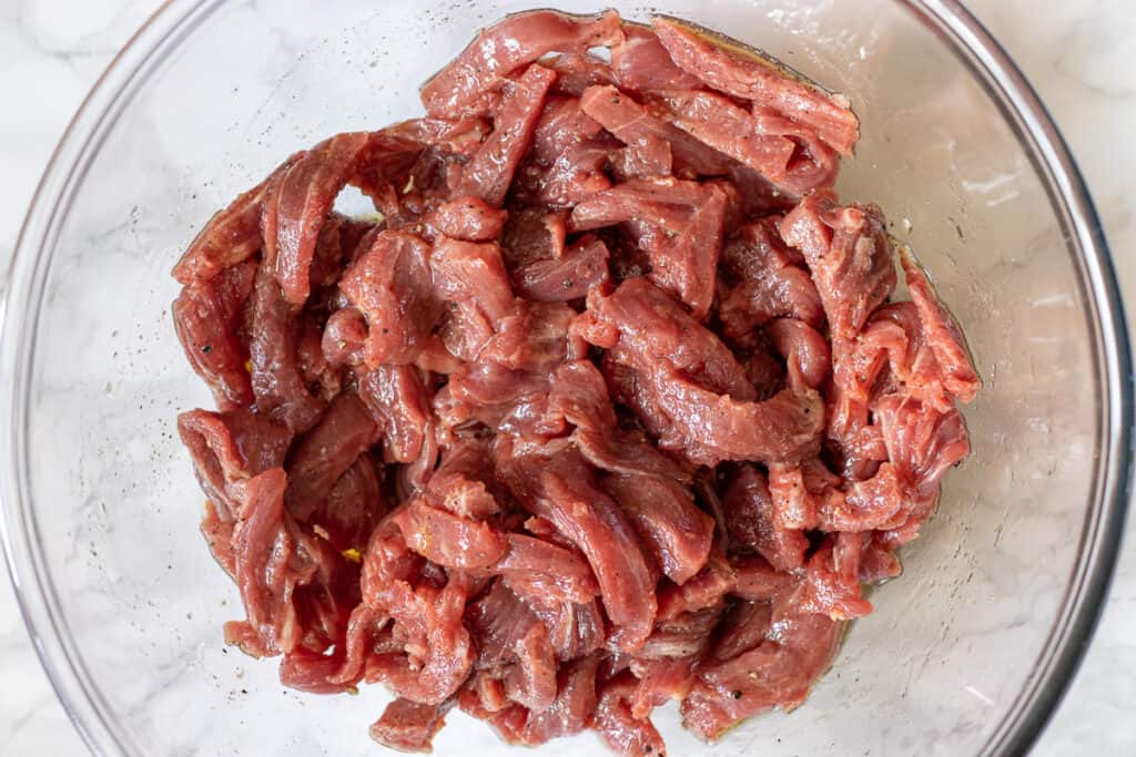 Julienne-cut beef is marinated in a bowl.