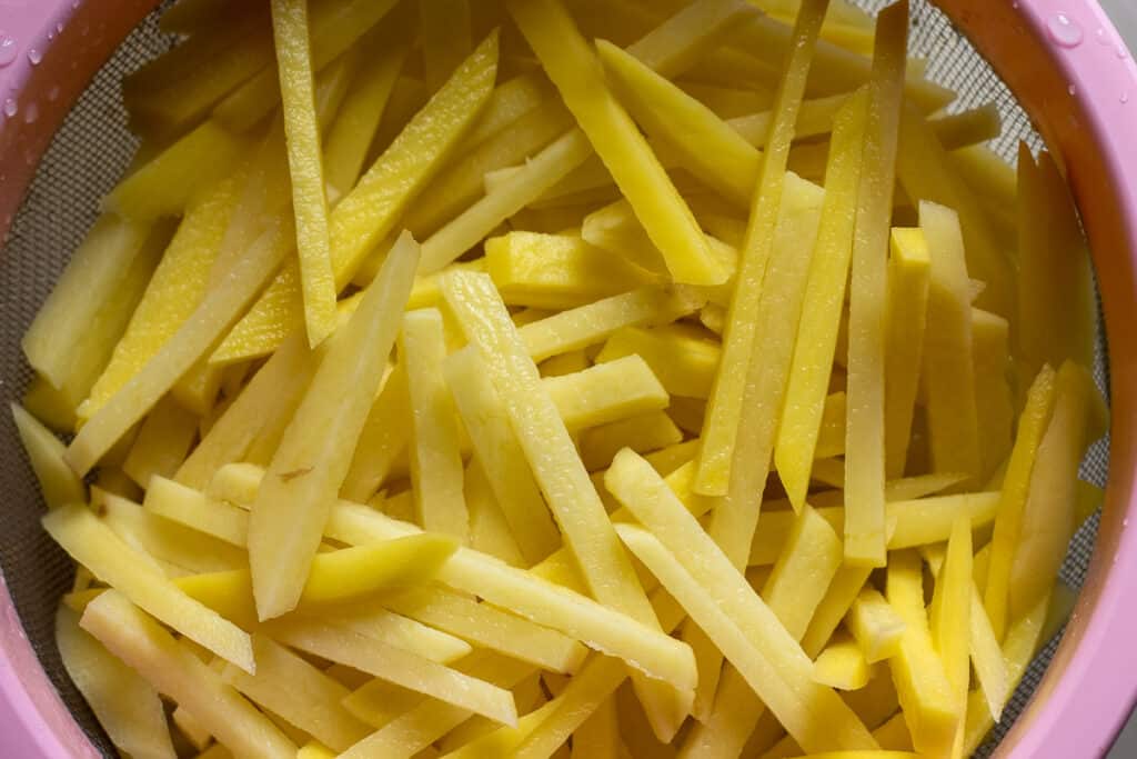 The matchstick potatoes are drained in a colander.
