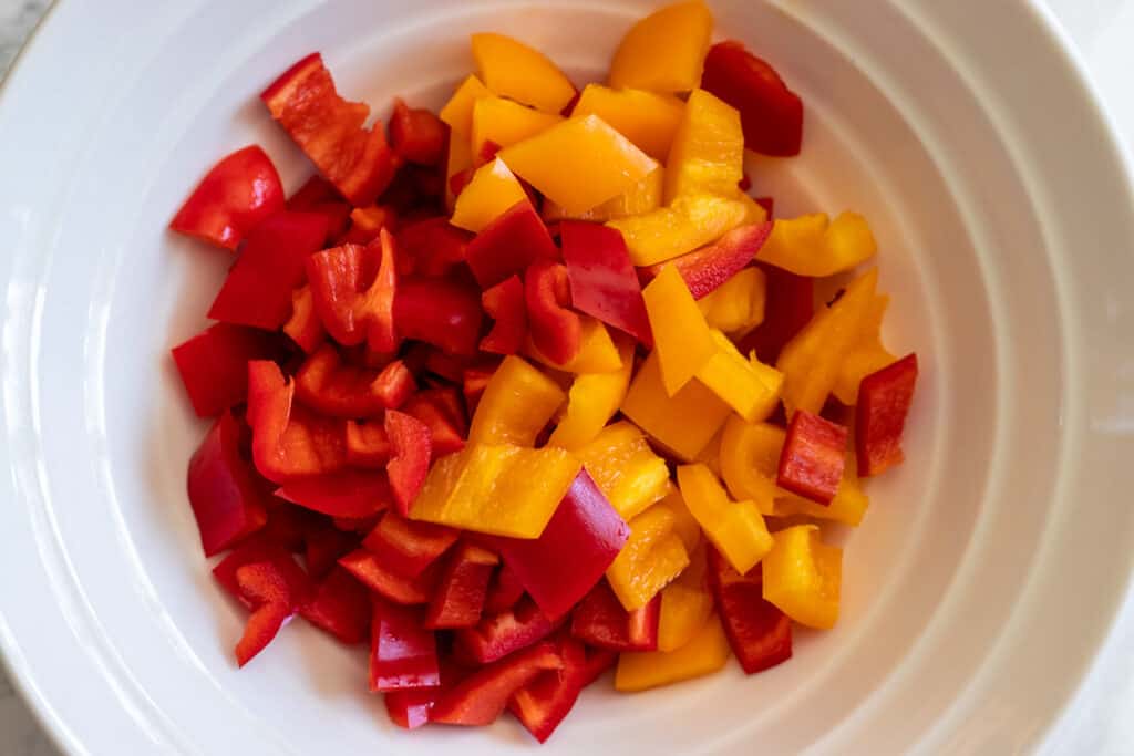 Diced red and yellow bell peppers in a white bowl.