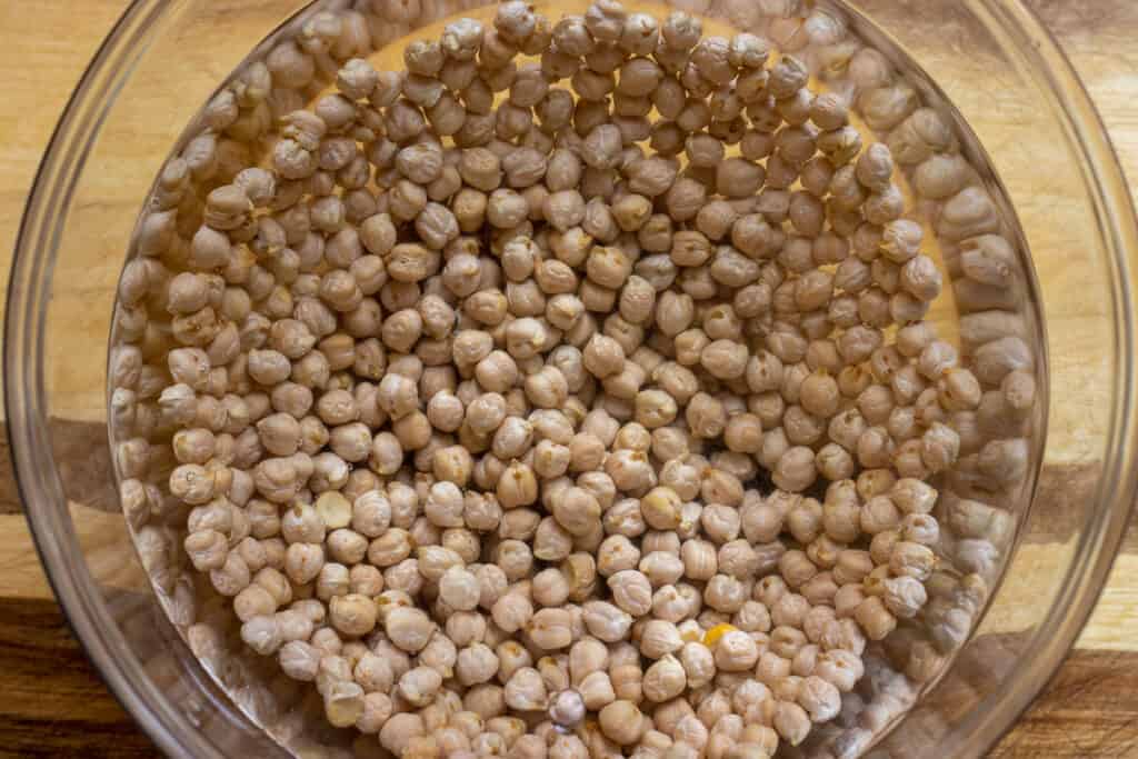 Dried chickpeas covered with water in a glass bowl.