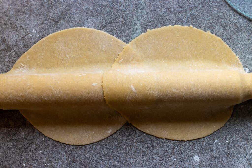 Two rolled dough circles lifted on a rolling pin.