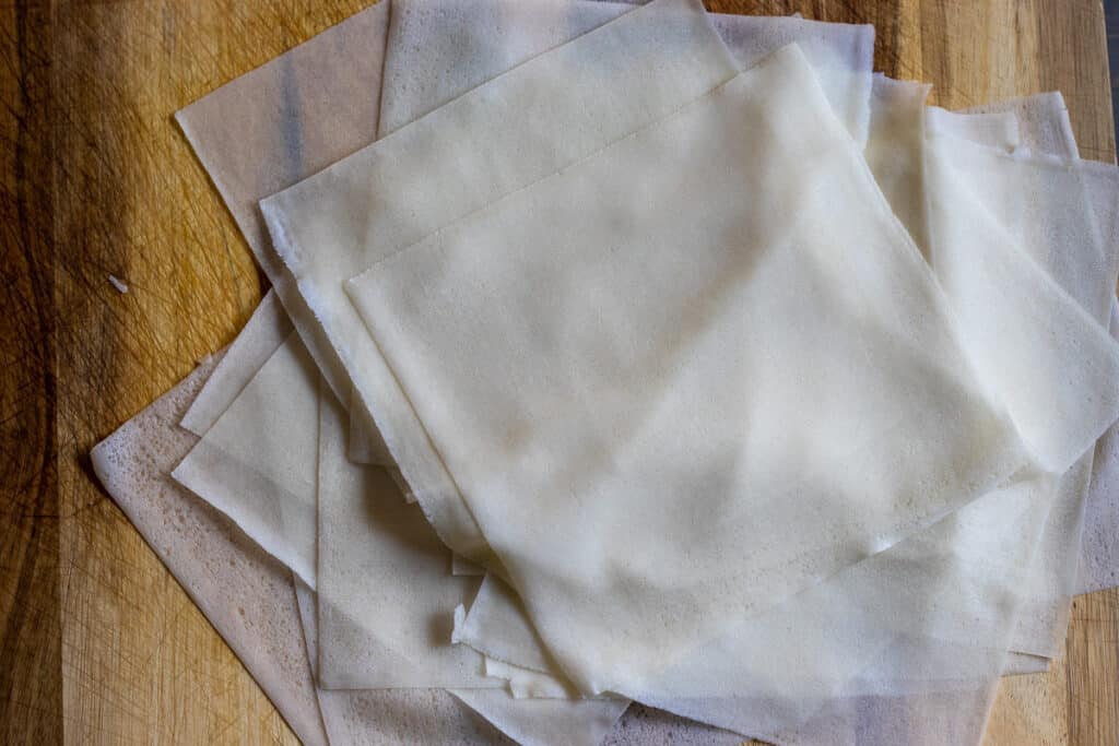 Square spring roll wrappers separated and covered with a damp kitchen towel.