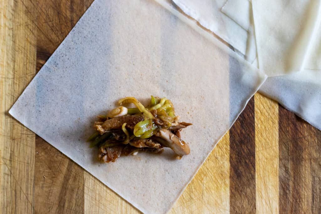 A square spring roll wrapper placed in a diamond shape with duck filling along the bottom corner.