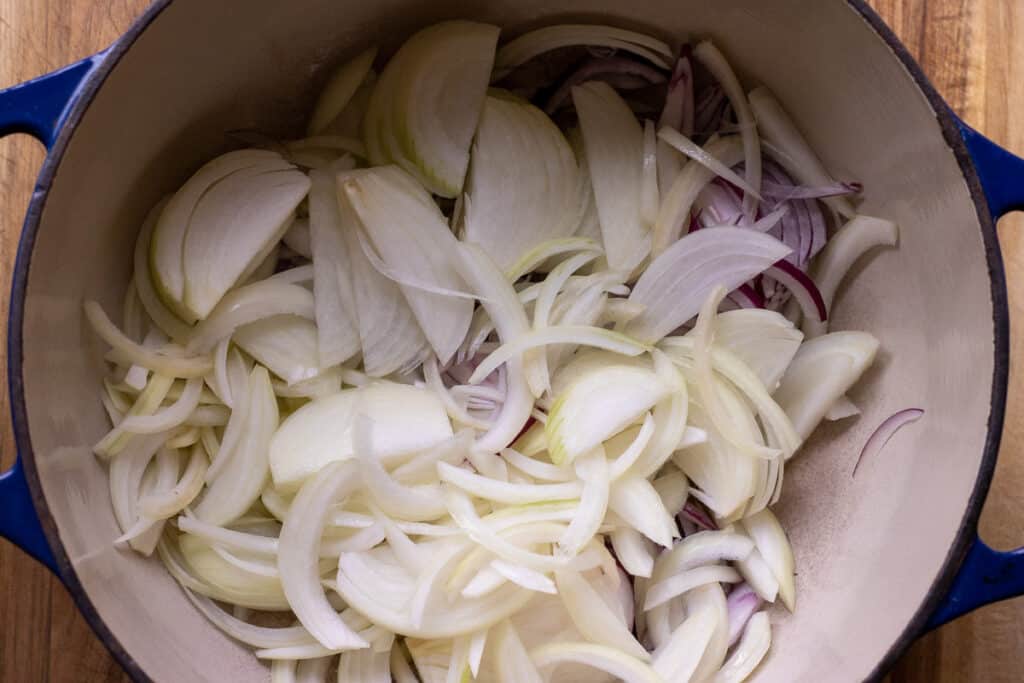 Sliced yellow and red onions added to melted butter in a Dutch oven.