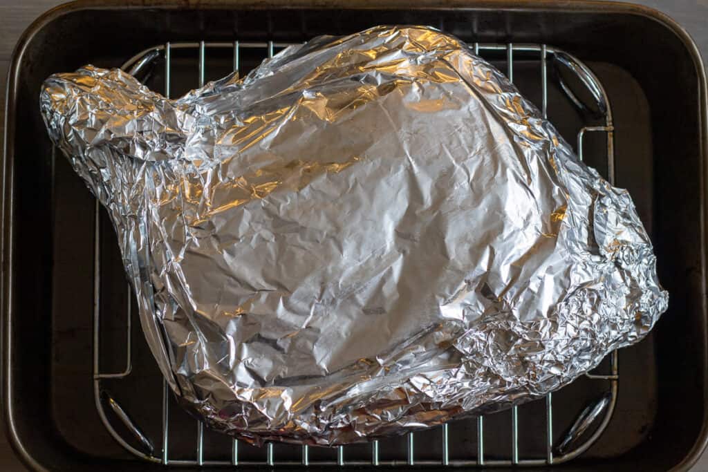 Lamb shoulder wrapped in tin foil and placed on a rack.