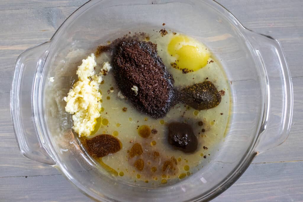 Spices, lemon juice, garlic, and olive oil are placed in a large bowl.