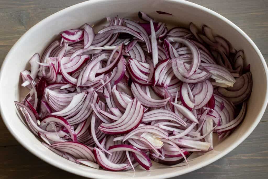 Sliced red onions are placed in a baking dish.