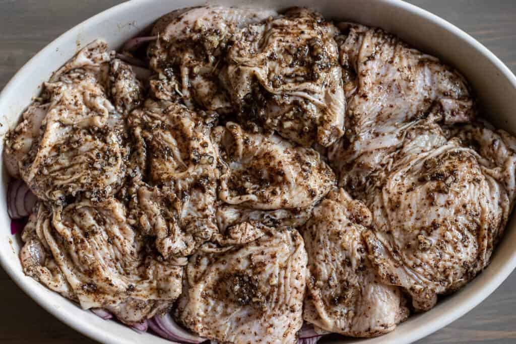 Marinated chicken pieces are placed on top of the onions.