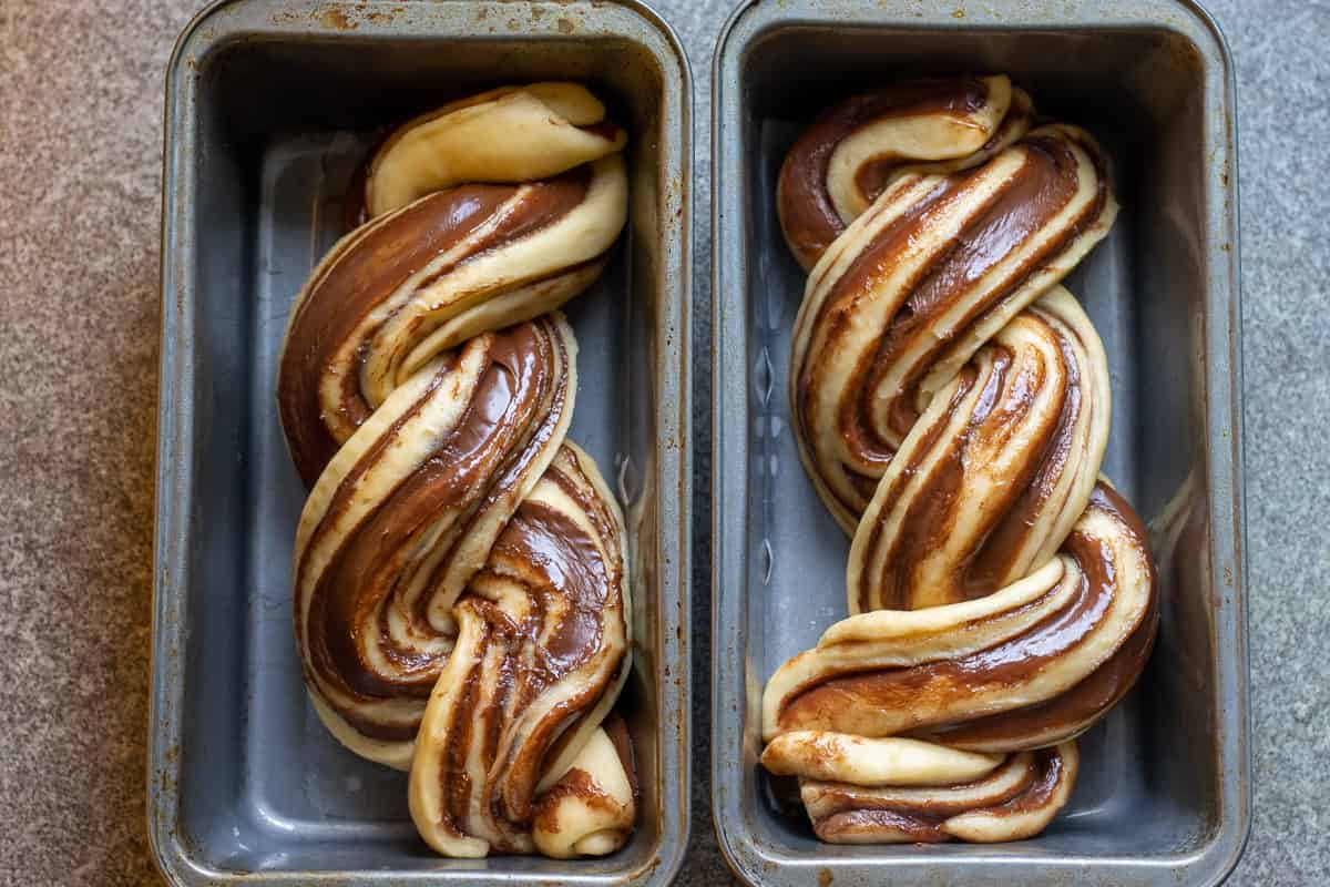 Shaped babka loaves rising in two baking pans.