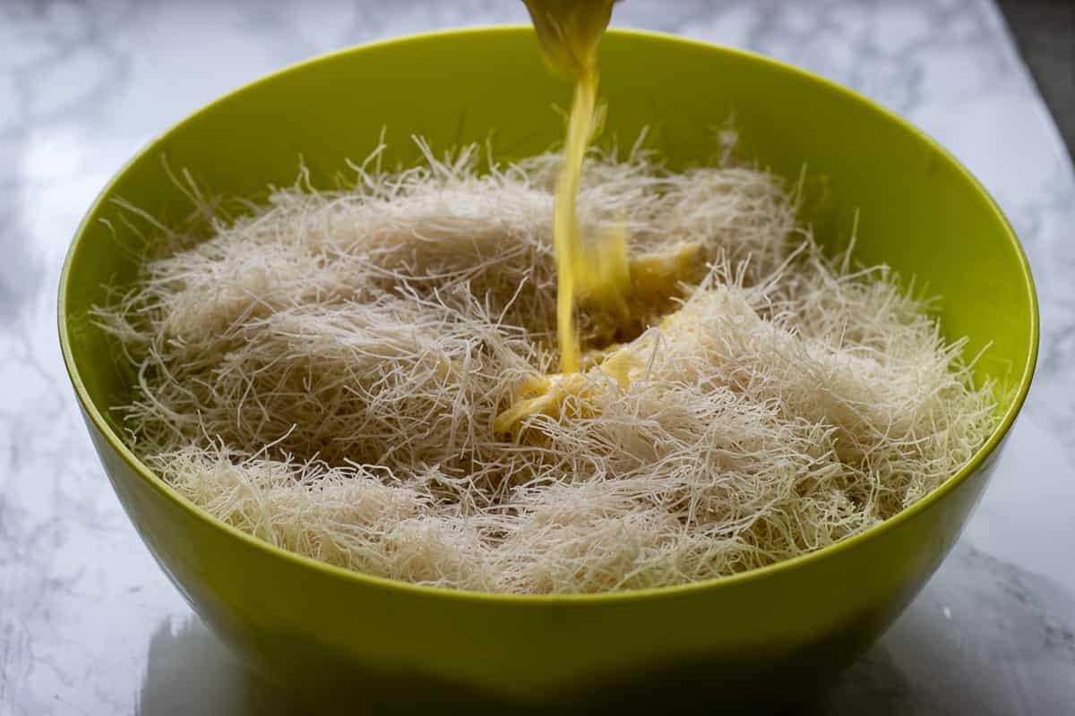 Pouring melted butter on kadaif pastry.