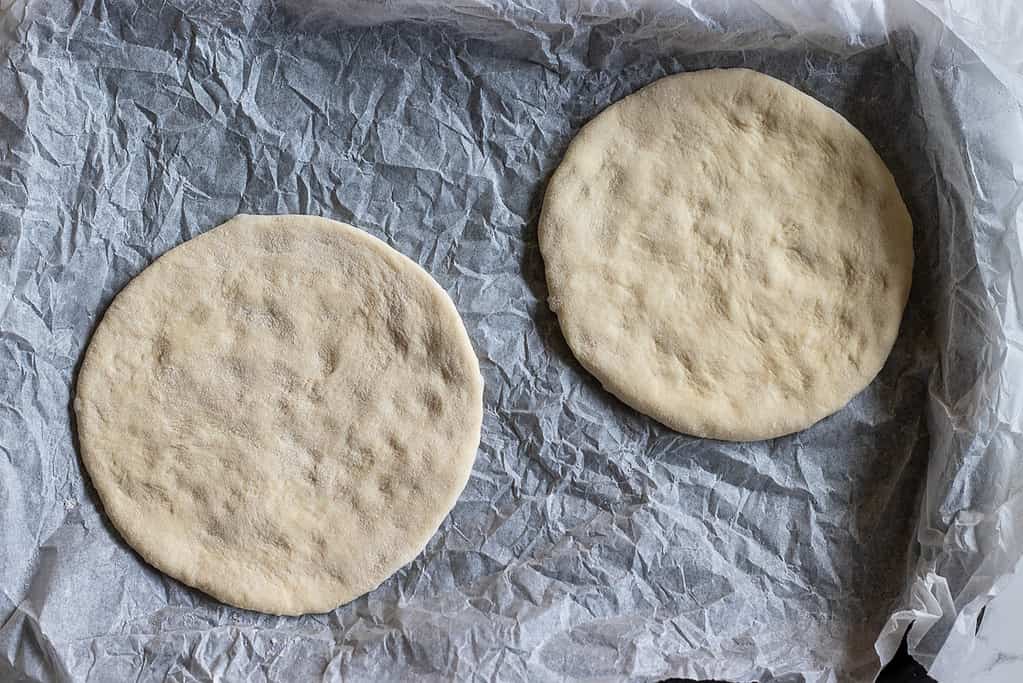 Two dough circles with fingertip dimples on a lined baking sheet.
