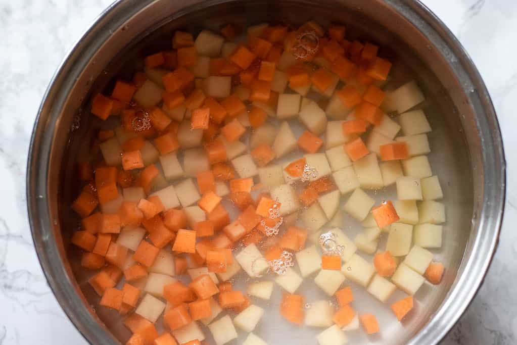 Diced carrots and potatoes in a pan filled with water.ar