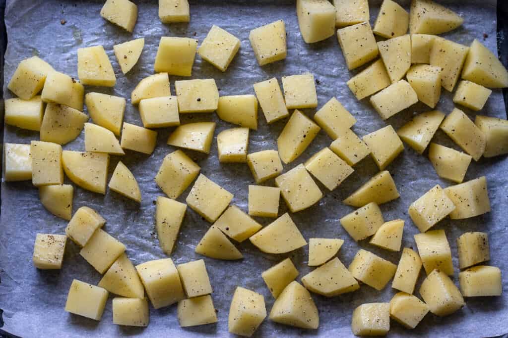 Potato cubes are drizzled with oil and seasoned with salt and pepper.
