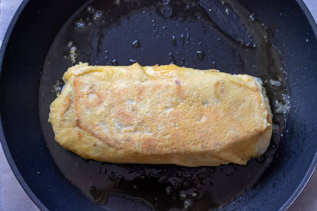 A piece of burrito is covered with melted cheese.