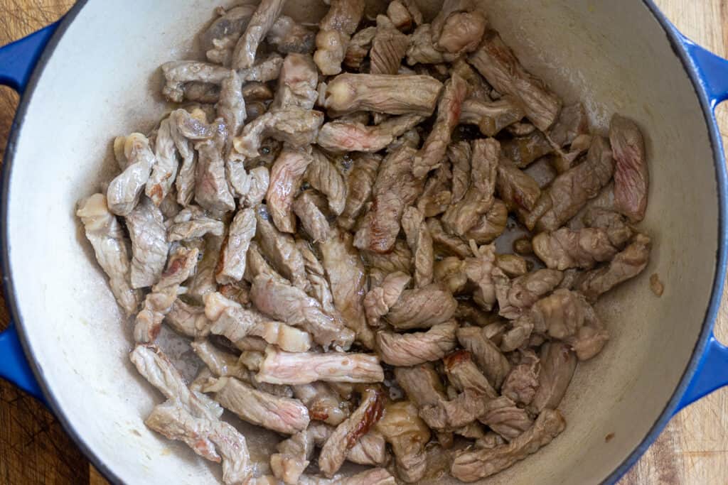 Sautéing sliced beef in a Dutch oven.