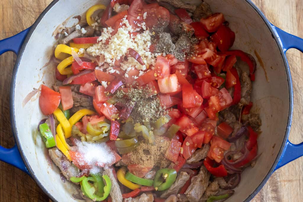 Chopped tomatoes, garlic, and seasoning are added to the pan.