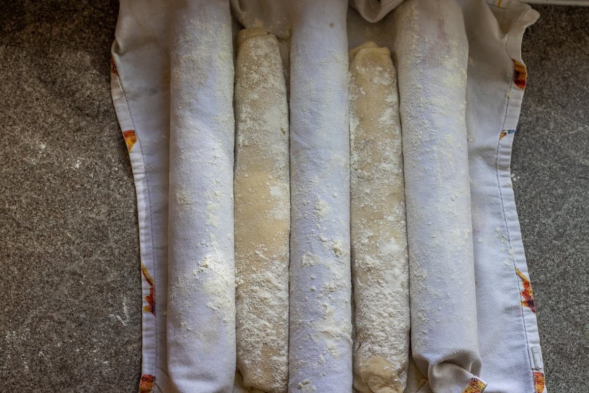 Bread loaves are placed on a kitchen towel for a second rise.