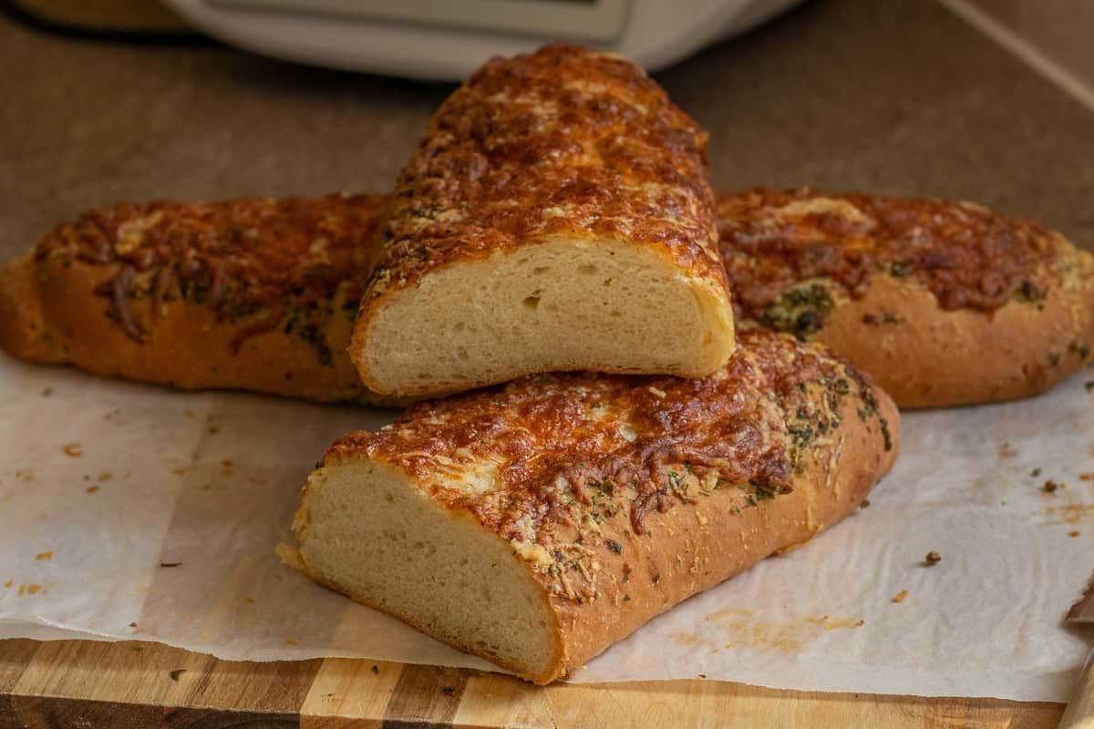 Two loaves of Italian cheese and herb bread, 1 cut in half.