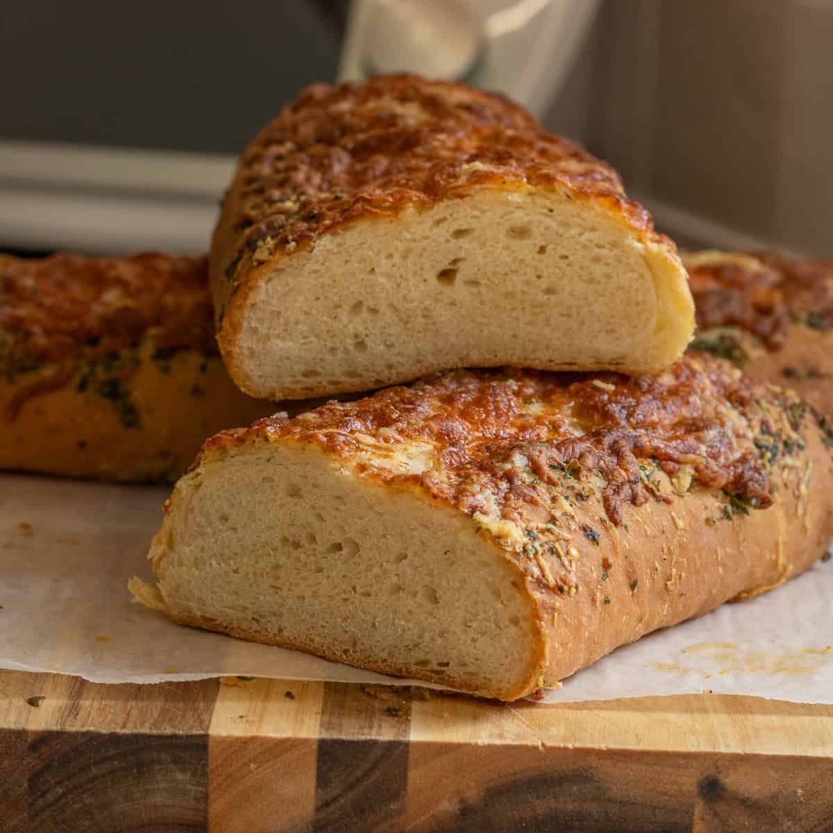 Two loaves of Italian cheese and herb bread, cut in half on a wooden board.