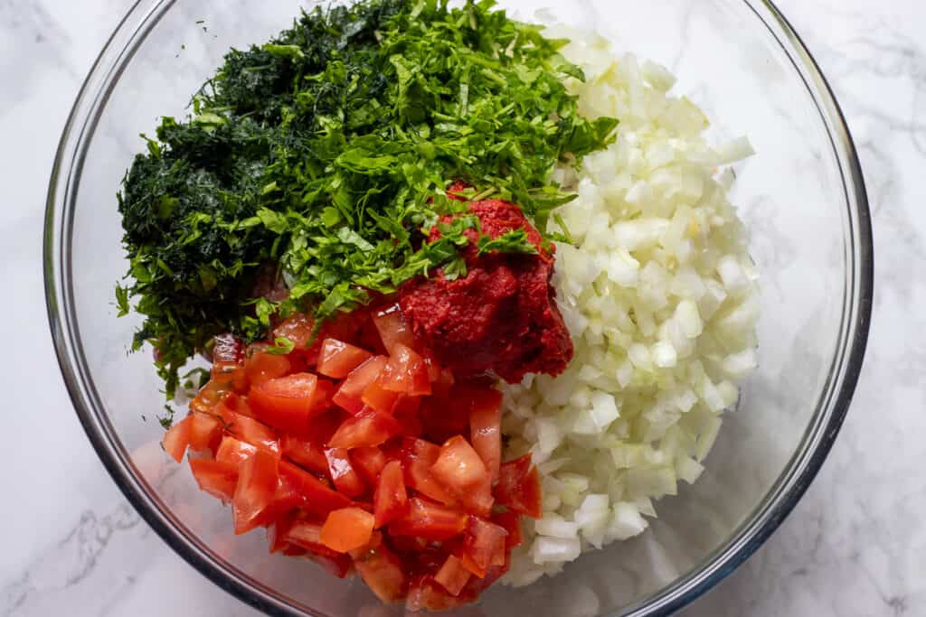 Tomatoes, herbs, onions, ground beef, and rice in a bowl.