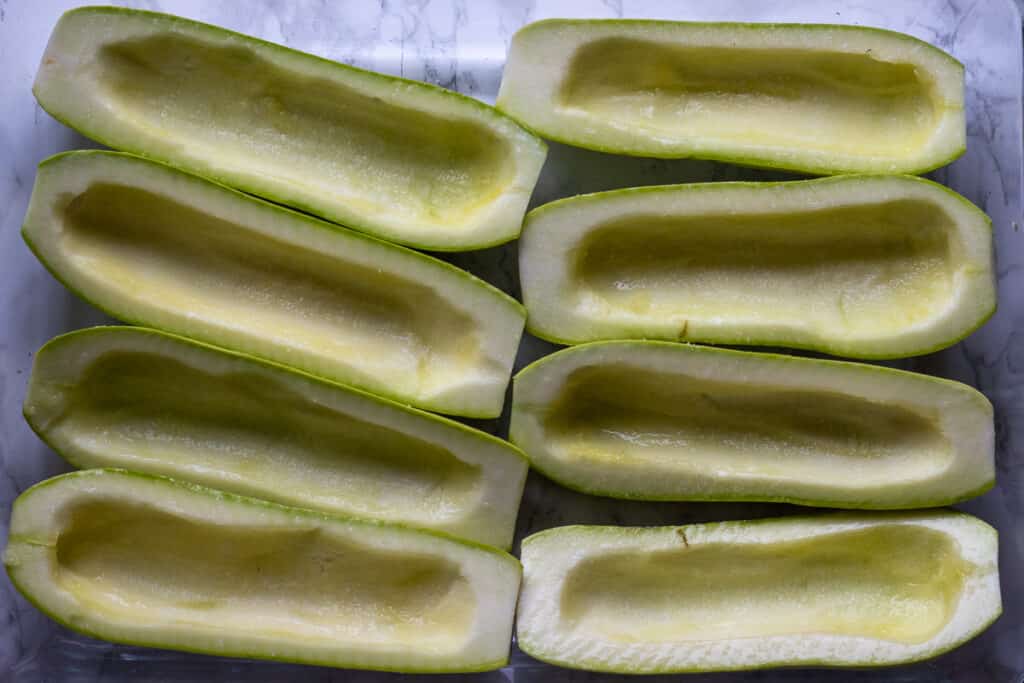 Hollowed zucchini boats in a baking dish.