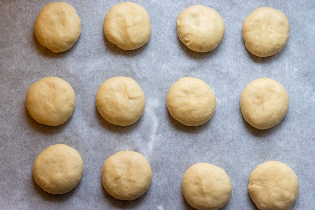 Twelve dough balls resting on a tray for the second rise.