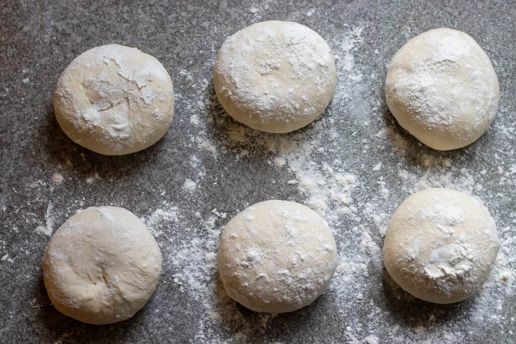 Six equal dough balls resting on a floured worktop.