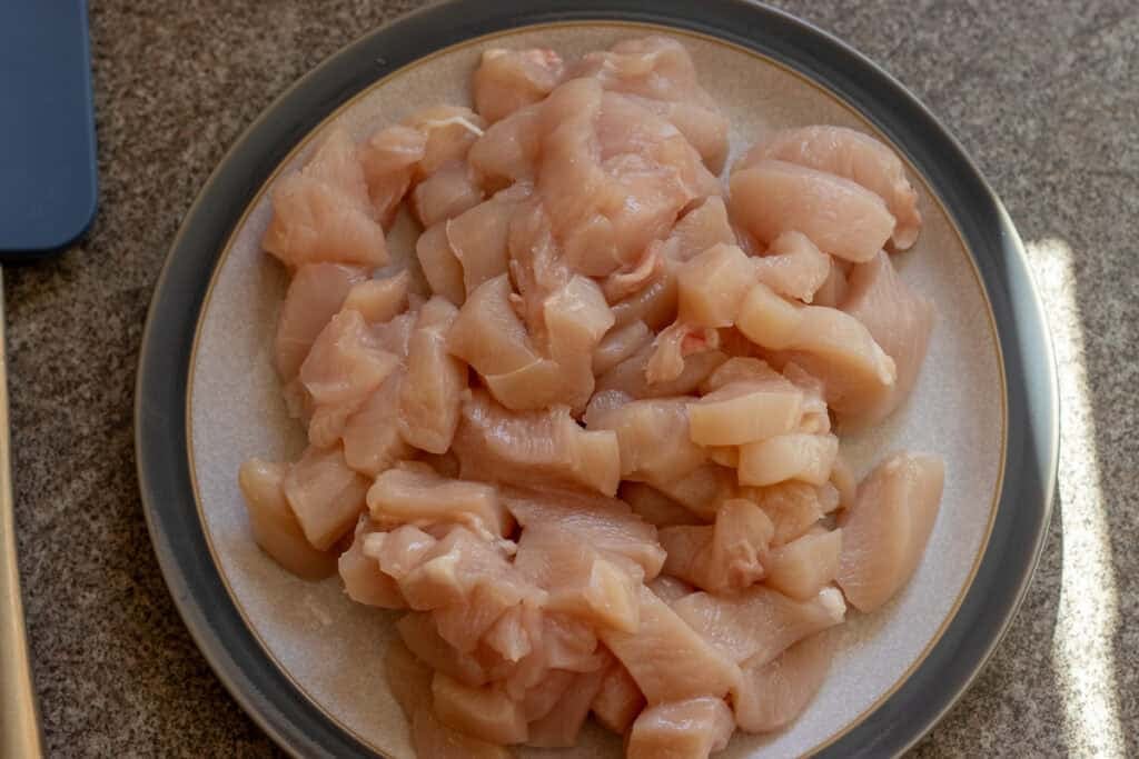 Raw bite-size chicken pieces on a plate.