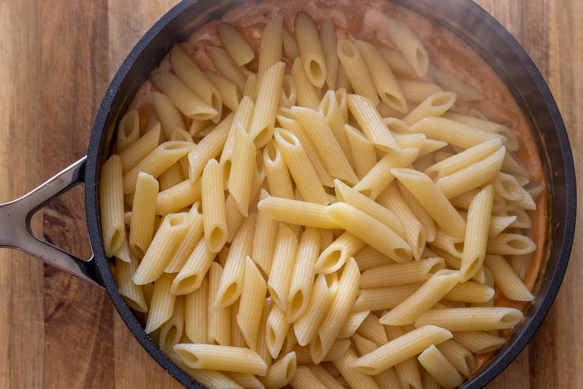 Cooked penne added to the skillet of creamy sauce.