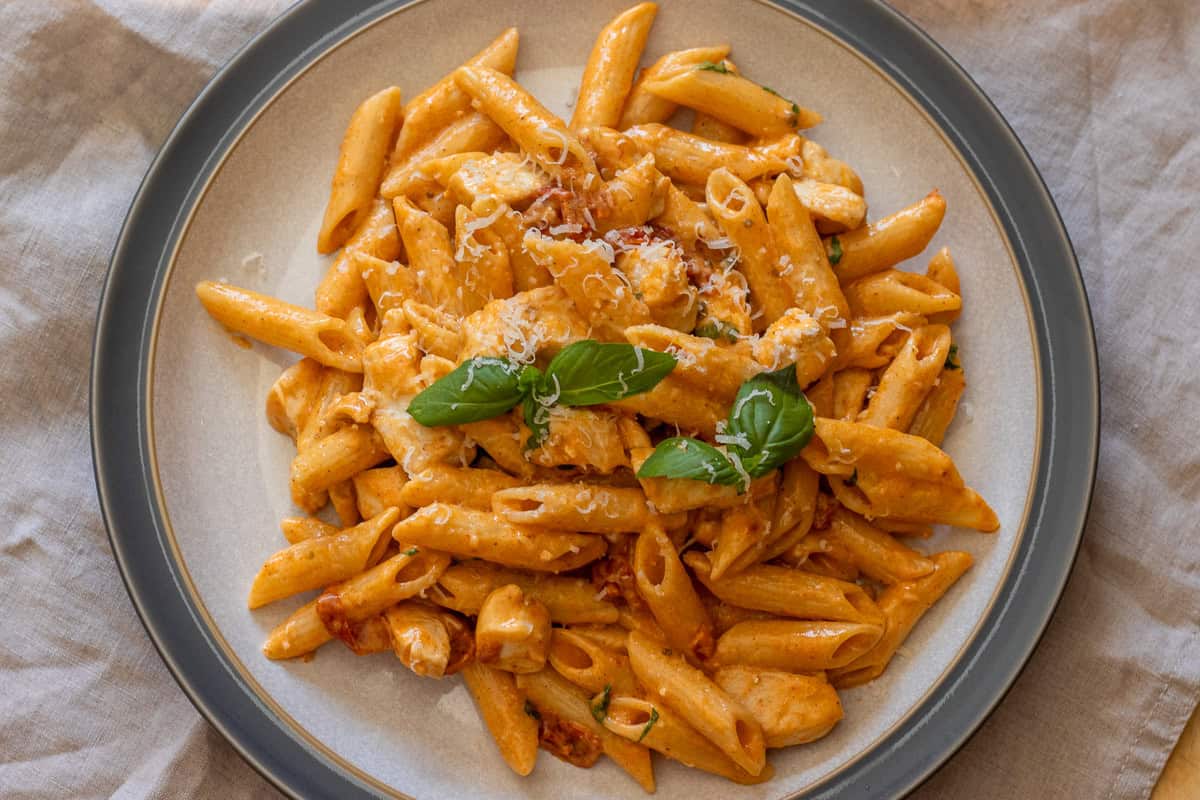 Overhead view of the finished penne dish topped with fresh basil and grated parmesan.