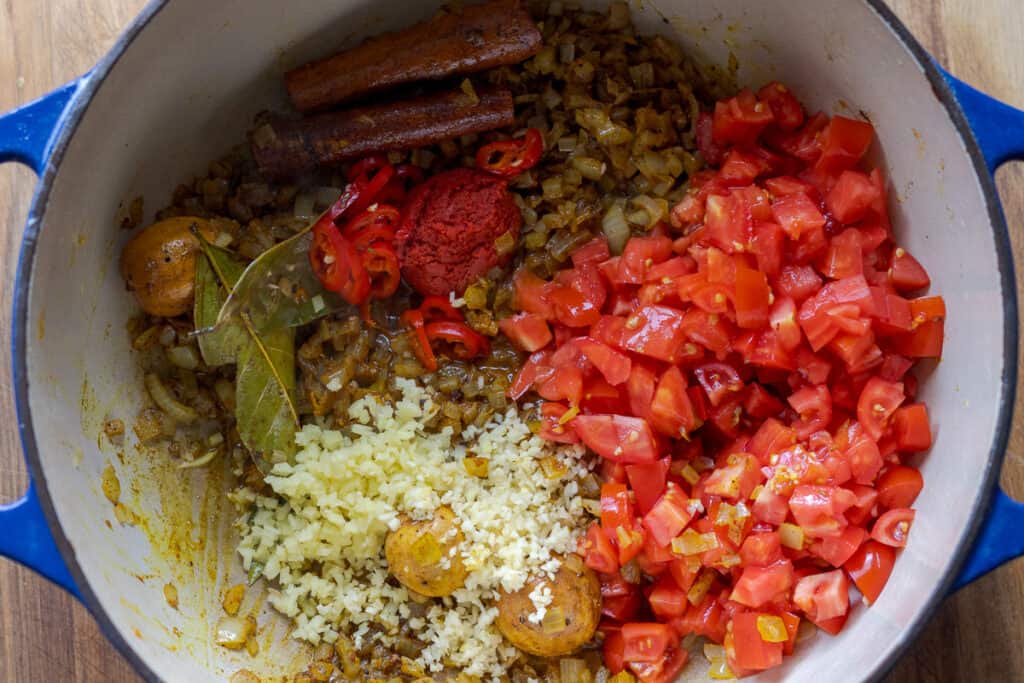 Ginger, garlic, tomato paste, and tomatoes are added to the pan.