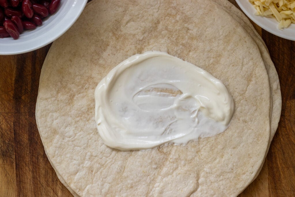 A dollop of sour cream is placed in the centre of a tortilla wrap.