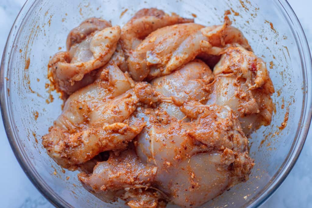 Boneless chicken thighs coated in shawarma marinade in a glass bowl.