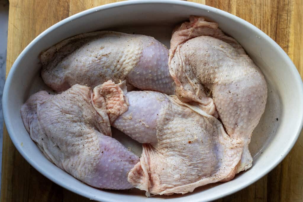 Seasoned chicken leg quarters in a baking dish.