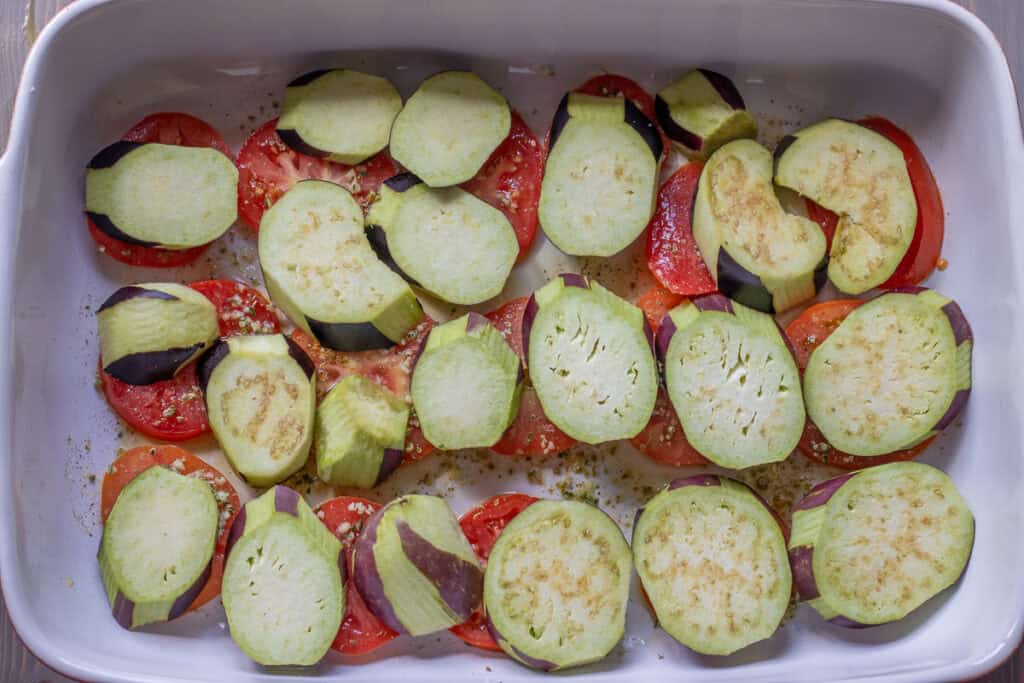 Sliced eggplants are arranged on top of sliced tomatoes.