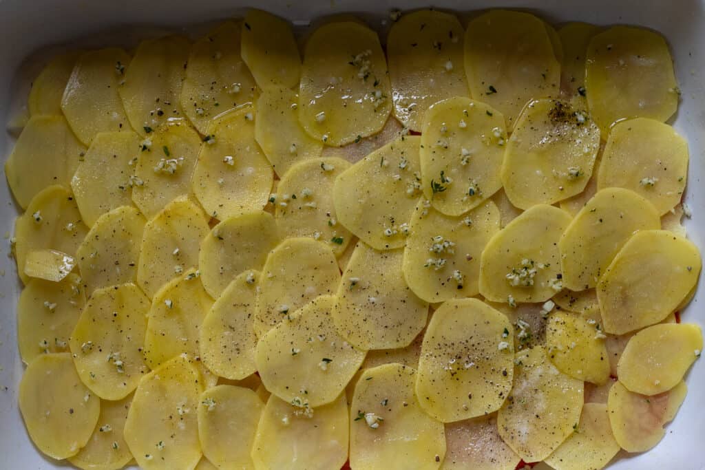 Sliced potatoes layered over the tomatoes, sprinkled with garlic and herbs.