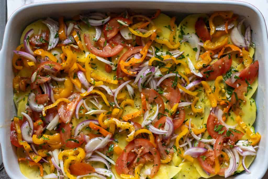 Sliced peppers and red onions sprinkled over potatoes.