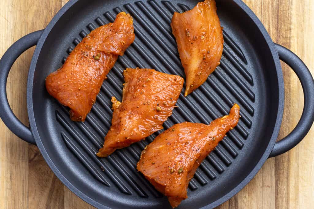 Marinated turkey tenderloins searing in a hot skillet before baking.