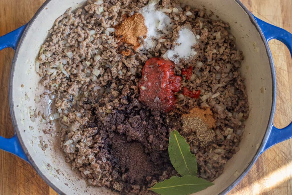 Tomato paste, seasoning, bay leaves, and a stock cube added to the pan.