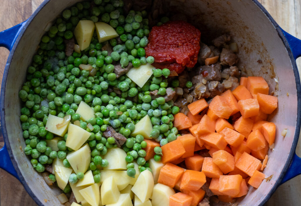 Green peas, potatoes, carrots, and tomato paste added to the pan.